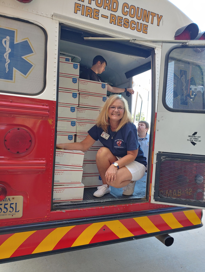 photo of smiling woman in ems vehicle filled with care packages to be sent to military members